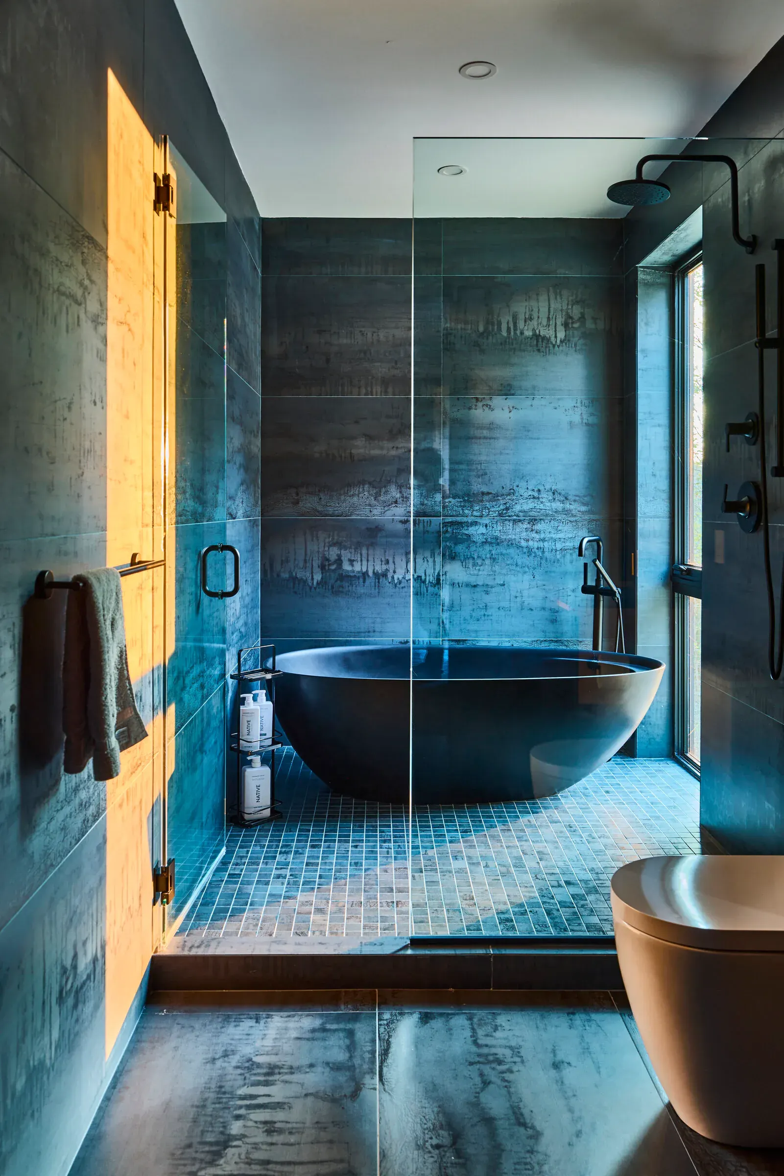 Verdant Sound primary bathroom — black soaking tub, raw concrete tile, glass shower