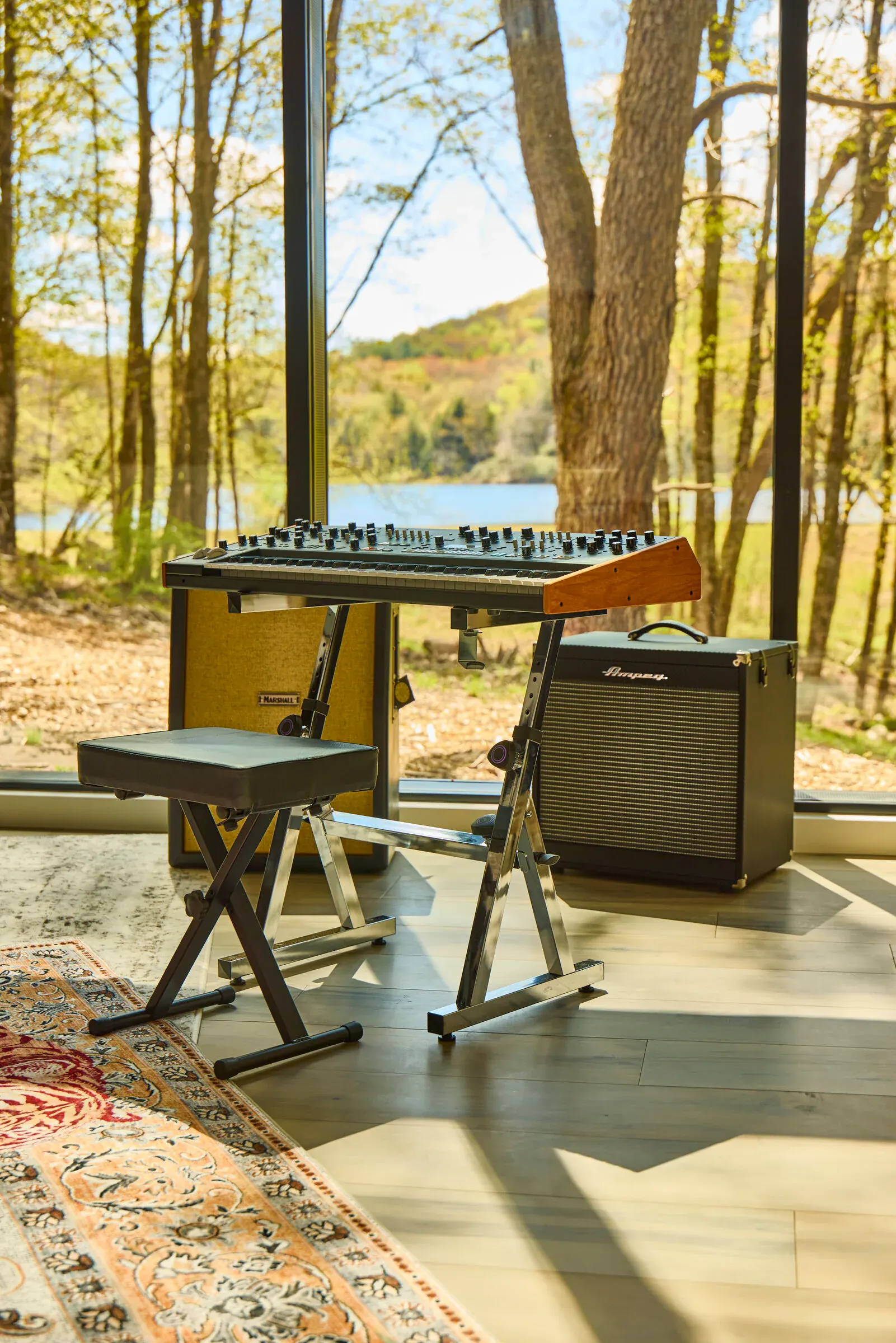 Synthesizer and keyboard station by the glass wall at Verdant Sound, lake visible through the windows