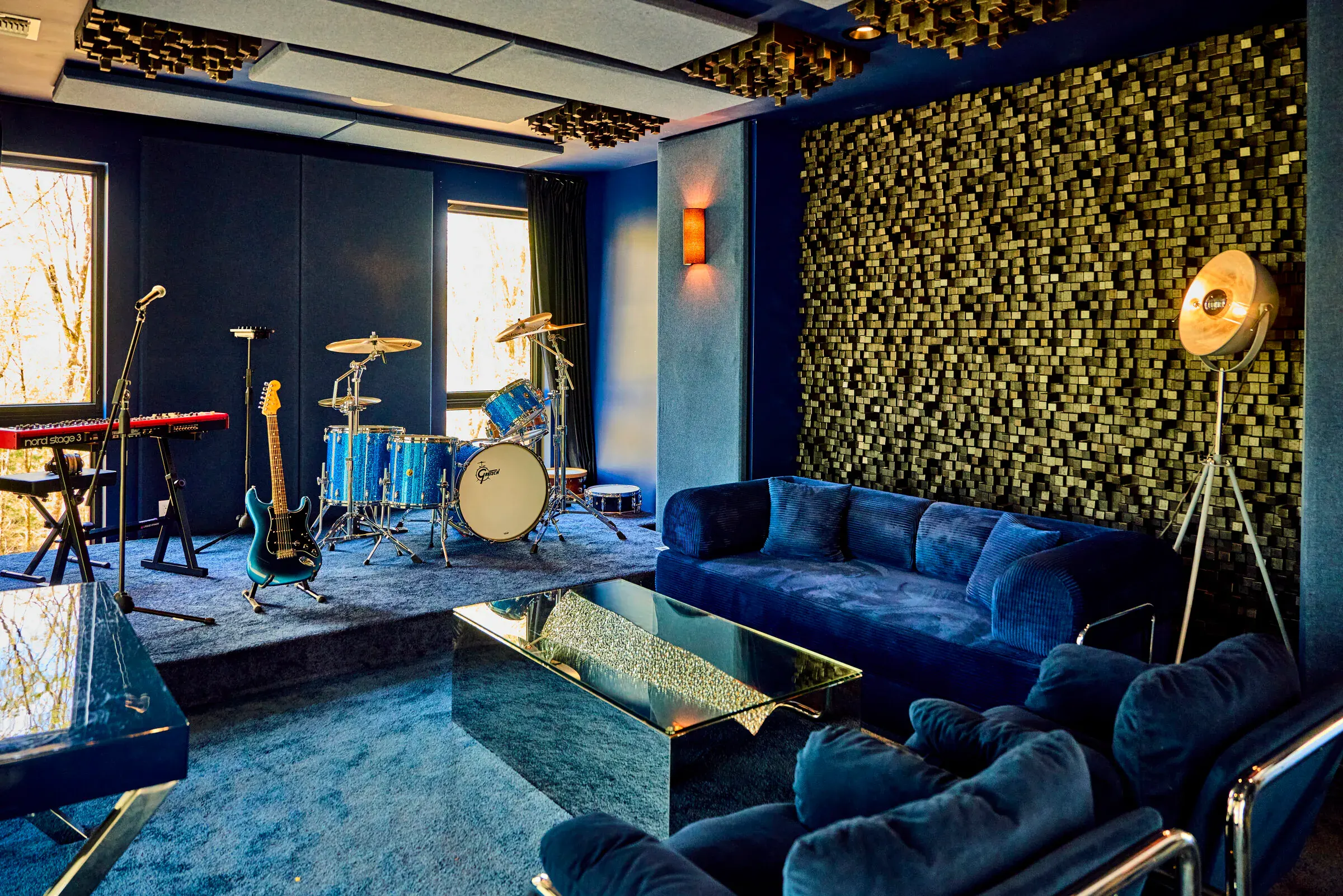 Verdant Sound lounge — fully treated secondary live room with stage, drum kit, blue velvet sofas, and gold acoustic wall
